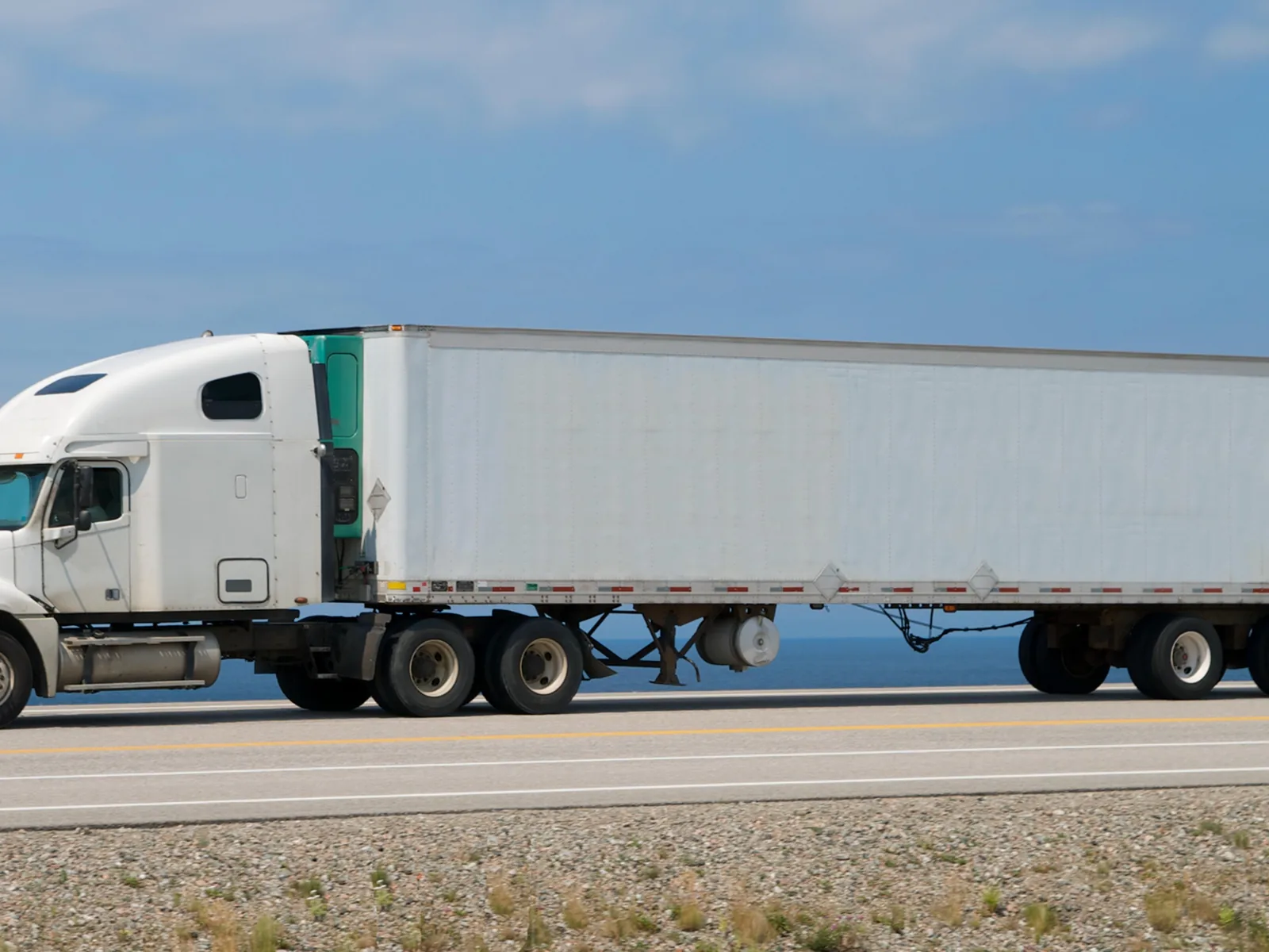 A white tractor pulling a white dry van trailer on the highway